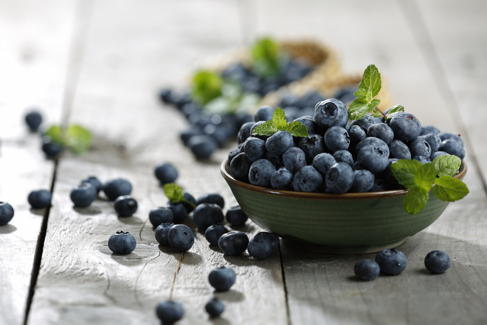 Bowl of blueberries with mint on a wooden table.