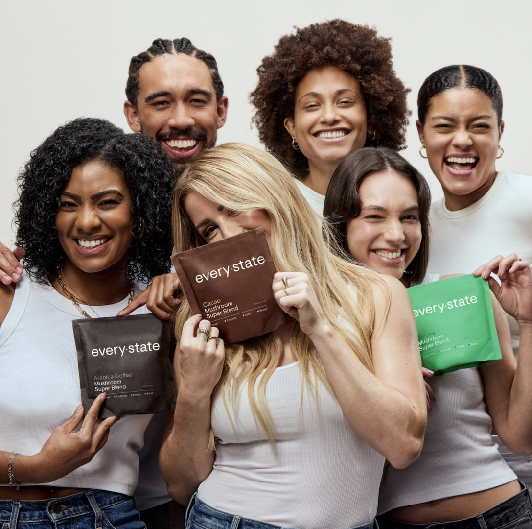 Ellie Goulding and a group of diverse people holding packets of every.state mushroom super blend.